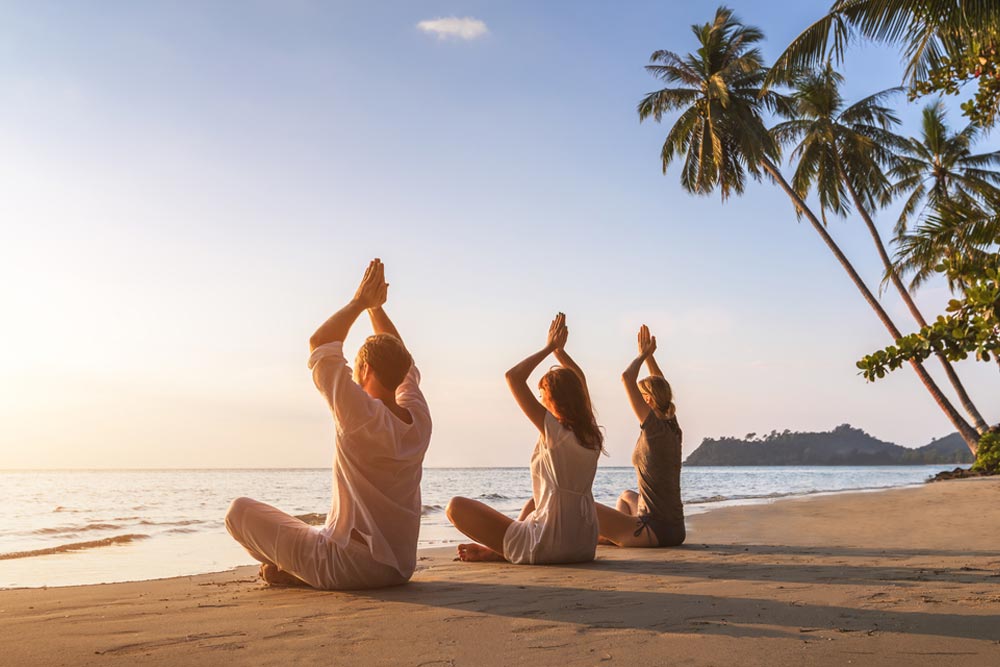Group of three people practicing yoga at beach